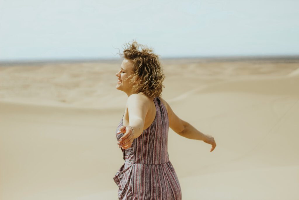 woman in white and purple stripe tank dress standing on brown sand during daytime